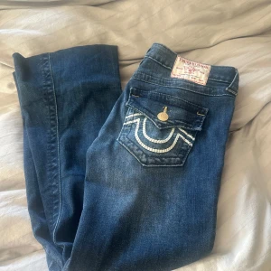 True Religion blå bootcut jeans - Snygga blå jeans från True Religion med bootcut passform och coola kontrastsömmar på bakfickorna. Modellen heter Joey LR flare braided hs flap. Storlek 25. Uppsydda till en som är 1.60-1.63 ungefär. Anv en kort stund för de är för stora för dottern på 14 år. Jeansen är i nyskick. Slutsålda på de flesta sidorna. Dyra i inköp 