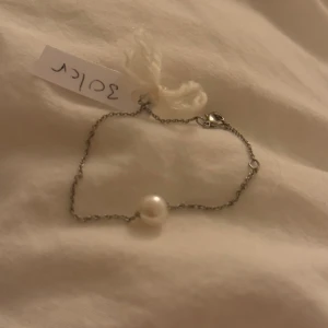 Armband med pärla - Stilrent armband i silverfärgad kedja med en rund vit pärla som detalj. Kedjan är tunn och har ett klassiskt lås. Perfekt för dig som gillar minimalistiska smycken med en elegant touch.