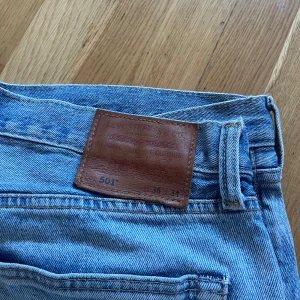 Levi's 501 ljusblå jeans 36/34 - Klassiska Levi's 501 jeans i ljusblå denim. Rak passform med fem fickor, knappgylf och ikonisk läderpatch bak i midjan. Perfekta för en avslappnad och tidlös stil. Storlek 36/34.