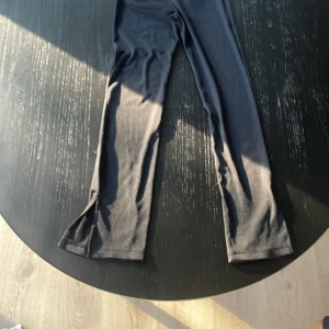Svarta ribbade leggings med slits - Säljer ett par svarta ribbade leggings med slits nertill på benen. De har en tight passform och är gjorda i ett stretchigt material som sitter snyggt. Perfekta för dig som gillar en stilren och trendig look.