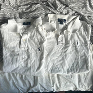 Polo Ralph Lauren pikér  - Två klassiska vita pikétröjor från Ralph Lauren med broderad logga på bröstet. Tröjorna har krage, knappar framtill och är tillverkade i mjuk bomull. Perfekt för en clean och stilren look. Är i storlek XL för barn vilket är ungefär xs-s i vanlig storlek. Är i bra skick 7/10 
