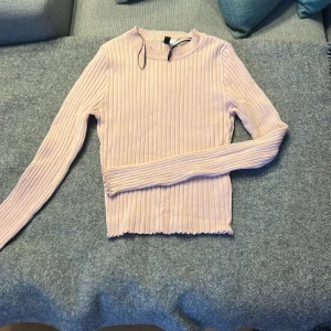 Ljusrosa ribbad tröja från H&M - Säljer en ljusrosa ribbad långärmad tröja från H&M i storlek S. Tröjan har en croppad passform med vågig kant nedtill och är tillverkad i mjuk stickad bomullsmix. Perfekt för dig som gillar enkel och snygg stil med lite edge.