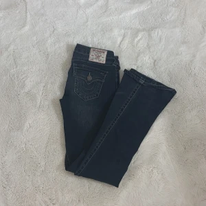 True Religion Joey Low Rise Flare Jeans - Mörkblå jeans från True Religion, modell Joey Low Rise Flare. Snygga kontrastsömmar, klassiska fickor med lock och knappar bak samt låg midja. Jeansen har bootcut/flare passform och är tillverkade i slitstarkt denimtyg.