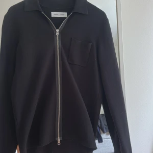 Svart ullkofta med dragkedja Samsøe - Svart kofta från Samsøe Samsøe i ull med silverfärgad dragkedja framtill, klassisk krage och en bröstficka. Långärmad och stilren modell som passar perfekt till lager-på-lager. Enkel och clean look.