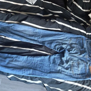 Grant Relaxed Tapered blå jeans 33/34 - Säljer ett par blå jeans från Grant i modellen Relaxed Tapered. De har klassisk femficksdesign, orangea sömmar och en avslappnad passform som smalnar av mot ankeln. Jeansen är tillverkade i slitstarkt denim och har knappgylf samt bälteshällor.