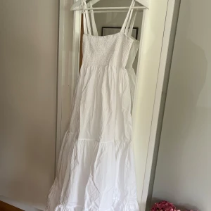 Vit långklänning  - Superfin vit långklänning med smockat liv och breda axelband. Klänningen har volanger nertill. Från ZARA, storlek M. Aldrig använd själv men köpt begagnad. Mycket fint skick, inga fläckar eller andra tecken på användning! 
