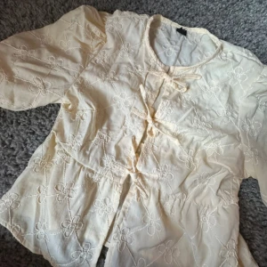 Broderad blus med knyt från SHEIN - Supersöt ljusgul blus från SHEIN med broderade blommor över hela tyget. Blusen har tre knytningar framtill, rund halsringning och lite puffiga ärmar. Perfekt för dig som gillar romantiska detaljer och en feminin vibe.