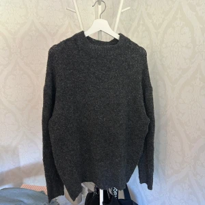 Mörkgrå stickad tröja från 157 - Mysig mörkgrå stickad tröja från 157 med enkel design och rund hals. Perfekt för lager-på-lager och chill dagar. Långärmad och i en lite loose passform som ger en avslappnad vibe.