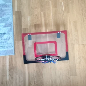 Basketkorg som man hänger på en dörr  - Ingen bok syns på bilderna, utan det som visas är en liten basketkorg med nät, perfekt för att spela basket hemma eller på kontoret. Den har en transparent bakplatta med röd och svart kant, och är enkel att montera på en dörr eller vägg.