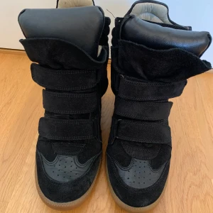 Isabel Marant svarta wedge sneakers - Svarta wedge sneakers från Isabel Marant med coola kardborreband och högt skaft. Skorna är i mocka och skinn med gummisula och har en dold kilklack för extra höjd. Perfekt för dig som vill ha en edgy och trendig look.