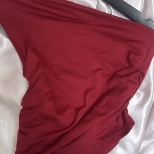 Vinröd topp i mjukt tyg - En enkel och stilren vinröd topp i mjukt och följsamt material. Perfekt för dig som gillar minimalistisk stil och vill ha något bekvämt men ändå snyggt. Toppen har en slät yta och är lätt att matcha med accessoarer.