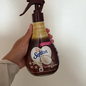 Rumsspray softlan coconut - Bilderna visar en flaska Softlan Coconut Spray, ett textilspray med kokosdoft för kläder och textilier.Den återstående mängden är från den hula delen o neråt.