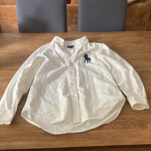 Vit skjorta från Ralph Lauren L - Klassisk vit skjorta från Ralph Lauren med stor mörkblå broderad polospelare på bröstet. Skjortan har lång ärm, knappar framtill och är tillverkad i mjuk bomull. Perfekt för en clean och stilren look.