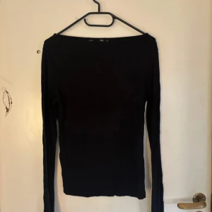 Svart långärmad topp från 157 - En stilren svart långärmad topp från 157, perfekt för dig som gillar enkel och clean look. Modellen är slim och har en rak, något bredare halsringning. Materialet känns mjukt och stretchigt, vilket gör den skön att bära hela dagen.