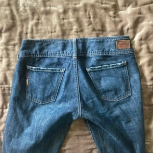 Blå Replay jeans med bootcut - Säljer ett par klassiska blå jeans från pepe jeans. Jeansen har dubbla knappar i midjan, fem fickor och snygga slitningar. Materialet är jeans i bomull och de har en mörkblå tvätt med lätt slitna detaljer. 