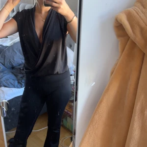 Svart omlottopp i satin-look - Snygg svart omlottopp med djup v-ringning och korta ärmar från mango. Toppen är i satin och perfekt att styla med både jeans och kostymbyxor. Storlek L men liten i storlek och passar mig som är en S-M