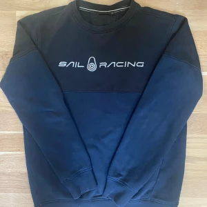 Mörkblå Sail Racing sweatshirt M - Mörkblå sweatshirt från Sail Racing i storlek M. Tröjan har broderad logga framtill och en mindre logga bak i nacken. Klassisk rund halsringning och långa ärmar. Tillverkad i mjuk bomullsmix, perfekt för en chill och sportig look.