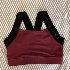 Vinröd sporttopp från Röhnisch - Vinröd sporttopp från Röhnisch med breda svarta axelband där loggan är invävd. Toppen har en stilren, tight passform. Osäker på storlek då lapparna är bortklippta men passar på mig som har xs. Säljs nytt för cirka 300kr.