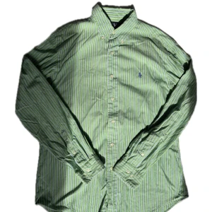 Ralph Lauren skjorta  - Snygg grön skjorta från Ralph Lauren med vita och blå ränder. Klassisk button-down krage, långärmad och med broderad blå logga på bröstet. Skjortan är i bomull och har knäppning framtill. Perfekt för dig som gillar preppy stil. Storlek 16 34/35