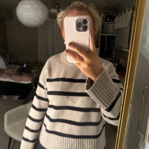 Beige och svart randig stickad tröja - Säljer en beige stickad tröja med svarta horisontella ränder. Tröjan har rund halsringning, breda ribbade muddar och lång ärm. Perfekt för dig som gillar en chill och klassisk look med lite oversized känsla.