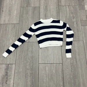 Randig croppad stickad tröja 157 XS - Snygg croppad stickad tröja från 157 i storlek XS. Tröjan har breda marinblå och vita ränder, ribbad struktur och långa ärmar. Perfekt för dig som gillar en trendig och avslappnad stil med lite edge.