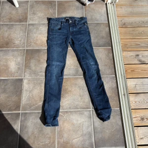 Blå Replay jeans, storlek 30 - Säljer ett par snygga blå jeans från Replay anbassa i storlek 30. Jeansen har klassisk femficksdesign, raka ben och tydliga Replay-detaljer på fickorna. Materialet är slitstarkt denim och färgen är mörkblå med lätt tvättad look.