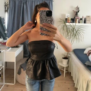 Svart axelbandslös topp - Snygg svart axelbandslös topp i skinnimitation med en peplumdetalj. Perfekt för en kväll ute eller en speciell tillställning. Toppen har en tight passform upptill och en lösare nederdel. Hör av er vid frågor🌸