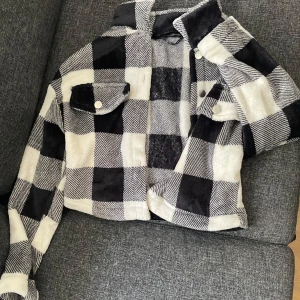 Svartvit rutig jacka - Säljer en cool svartvit rutig jacka med knappar och krage. Jackan har en croppad passform och är fluffig.