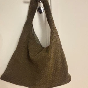 Olivgrön axelväska i flätat material - Säljer en olivgrön axelväska i ett snyggt flätat material. Har använt några få gånger, så den är i väldigt fint skick