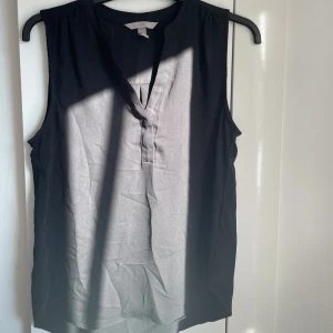 Svart ärmlös topp från H&M!! - Säljer en stilren svart ärmlös topp från H&M. Perfekt för lite extra elegans eller som ett lager under en kavaj. Toppen har en enkel design med en liten v-ringning framtill⭐️