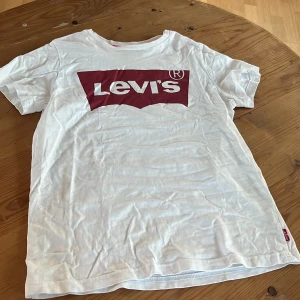 Vit t-shirt från Levi's - Säljer en klassisk vit t-shirt från Levi's med det ikoniska röda logotyptrycket på bröstet.  T-shirten har en normal passform och korta ärmar.
