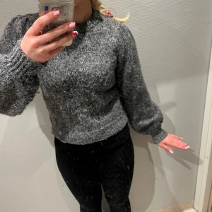 Grå stickad tröja - Säljer en mysig grå stickad tröja med puffiga ärmar och ribbade muddar. Perfekt för kyliga dagar. Tröjan har en klassisk rund hals och en bekväm passform.