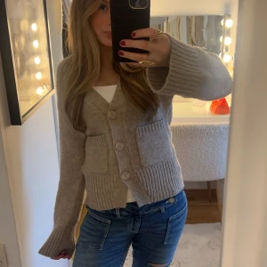 Beige stickad kofta - Säljer en mysig beige stickad kofta med stora knappar och två fickor framtill. Perfekt för kyliga dagar och ger en avslappnad look. Koftan har långa ärmar och en ribbad design vid ärmslut och nederkant. Är en Xs men passar en S/M då storlek är lite stor!🌸Säljer för ett lite dyrare pris då de är en stor favorit 