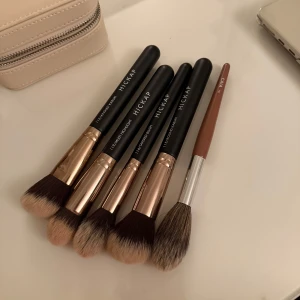 Set med sminkborstar från Hickap och caia  - Säljer ett set med fem sminkborstar från Hickap och en från caia. Inkluderar Angled Kabuki, Multi Highlight, Tapered Blush och Round Kabuki borstar från Hickap med svarta handtag och roséguld detaljer. En borste från caia med brunt handtag och silverdetaljer ingår också.
