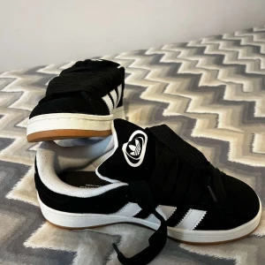 Svarta sneakers med vita detaljer - Snygga svarta sneakers från Adidas med vita ränder och logga. Skorna har en klassisk design med snörning och en bekväm passform. Perfekta för en avslappnad stil.
