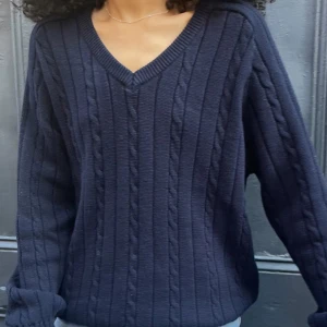Svart stickad tröja från Brandy Melville - Säljer en mörkblå oversized stickad tröja från Brandy Melville med v-ringning. Tröjan har ett klassiskt kabelstickat mönster och långa ärmar. Perfekt för en stilren och bekväm look.