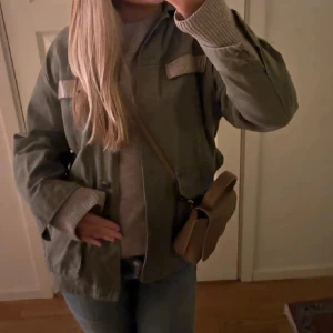 Grön jacka från Zara - Snygg grön jacka från Zara med glittriga detaljer på bröstfickorna. Jackan har en klassisk krage och knäppning framtill. Perfekt för en stilren look.