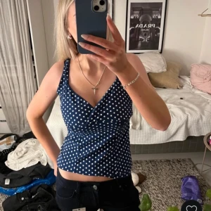 Blå prickig omlottopp - Säljer en snygg blå omlottopp med vita prickar. Toppen har en v-ringad design och smala axelband, perfekt för sommardagar. Den är både stilren och bekväm.