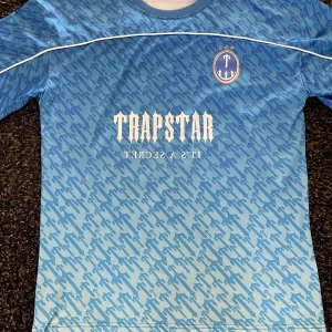 22 Jersey från Trapstar - Snygg Jersey från Trapstar med ett unikt mönster och vit text som passar perfekt till sommaren. Tröjan är i storlek S men passar mer som M