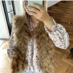 Brun pälsväst - Säljer en snygg brun pälsväst som är perfekt för att lägga till lite stil till din outfit. Västen har en fluffig textur och är ärmlös, vilket gör den idealisk för lager-på-lager-styling.