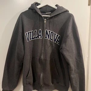 Grå hoodie från Champion - Säljer en grå hoodie från Champion med texten 'VILLANOVA' på framsidan. Tröjan har dragkedja och en klassisk huva. 