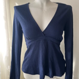 Mörkblå omlottopp med knytband - Snygg mörkblå omlottopp med v-ringning och långa ärmar. Toppen har ett knytband i ryggen för en justerbar passform. Perfekt för en stilren look. Prislapp kvar!