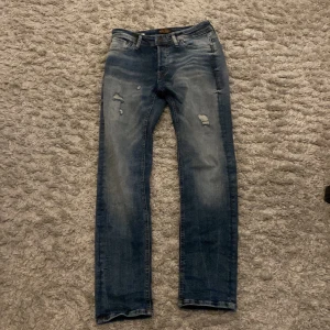 Blå jeans från Jack & Jones - Snygga blå jeans från Jack & Jones med slitna detaljer och en klassisk femficksdesign. Perfekta för en avslappnad stil. De har en dragkedja och knapp framtill.