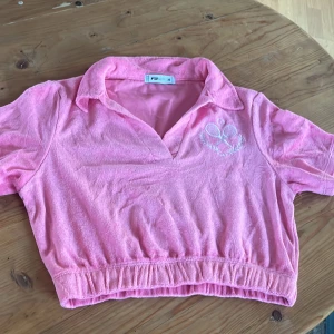 Rosa frotté pikétröja från New yorker - Säljer en rosa frotté pikétröja från New YORKER med korta ärmar och broderat märke på bröstet. Tröjan har en klassisk krage och elastisk nederkant. 