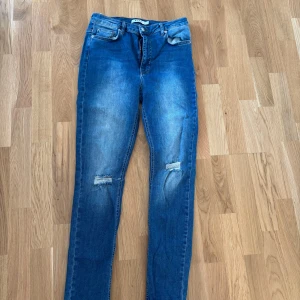 Blå jeans från NA-KD - Snygga blå jeans från NA-KD med slitningar på knäna. De har en klassisk femficksdesign och en knappgylf. Perfekta för en avslappnad stil. Super stretchiga ! 