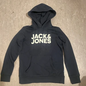Marin blå hoodie från Jack & Jones - Snygg marin blå hoodie från Jack & Jones med stor logga på framsidan. Tröjan har en klassisk känguruficka och en bekväm huva. Perfekt för en avslappnad stil.