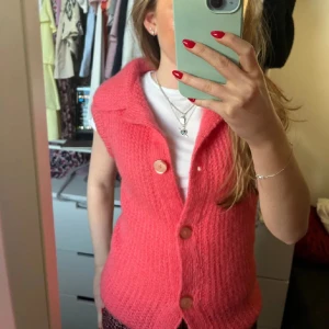 Rosa stickad väst med knappar - Säljer en snygg rosa stickad väst med stora knappar framtill. Västen har en klassisk krage och är perfekt för att lägga till lite färg i din outfit. Passar bra över en t-shirt eller blus.