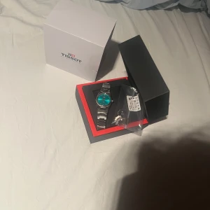 Tissot PRX turkos urtavla stål - Snygg Tissot PRX med turkos urtavla och stilren länk i rostfritt stål. Klockan har datumvisning och klassisk rund form. Kommer i originalbox med extra länkbitar. Perfekt för dig som gillar modern design och schweizisk kvalitet. Använd cirka 5-10 gånger inga defekter på klockan alls ser exakt ut som en ny från butik 