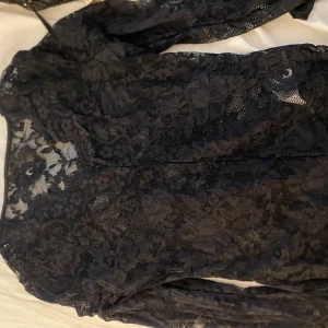 Svart blus med blommönster - Säljer en svart spettröja med långärmade ärmar och blommigt mönster. Blusen har en transparent look tack vare spetsen och är figurnära i modellen. Perfekt för dig som gillar detaljer och vill sticka ut med en elegant vibe.