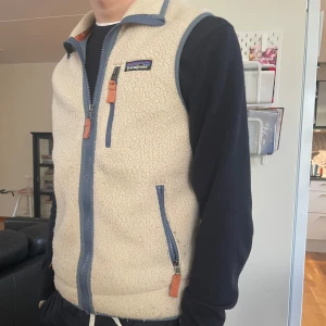 Patagonia väst - Säljer en beige fleeceväst från Patagonia med blå detaljer och dragkedjor. Perfekt att slänga över en hoodie för extra värme. Passar in bra nu till hösten. XS och modell 170cm 60kg. Lite nopprig därav pris.